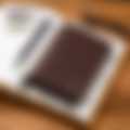 Two premium brown leather wallets placed on a gray surface, accompanied by a pen, showcasing a sophisticated handcrafted design.