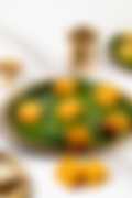 Bright orange squares of Indian sweet on a banana leaf–lined plate, with a brass lamp and cup in the background.