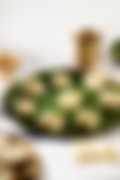 Squares of white Indian barfi topped with crushed pistachios on a banana leaf–lined plate, with a brass lamp and cup in the background.
