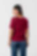 A woman wearing a maroon short-sleeve top with lace details on the shoulders and blue jeans, shown from the back against a white background.
