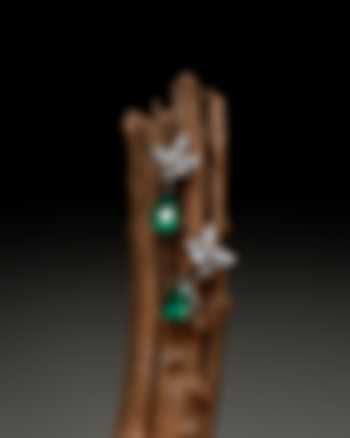 Exquisite drop earrings featuring pear-shaped emeralds and diamond clusters, displayed on a rustic wooden branch against a dark backdrop.