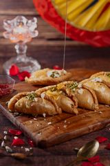 A plate of golden sweets made with almonds and pistachios, drizzled with honey, presented on a wooden board.