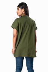 Woman wearing an olive green high‐neck tunic top with rolled sleeves, side slits, and blue skinny jeans, posing in three‐quarter profile.