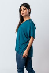 A woman wearing a teal short-sleeve top with lace shoulder details and blue jeans, posed in profile against a light grey background.
