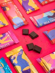 A partially unwrapped Fancis Fruit & Nut chocolate bar on a red background, surrounded by coffee beans, ground coffee, and cashews.