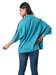 A woman wearing a loose teal top with wide sleeves, viewed from the back, paired with jeans on a white background, showcasing a relaxed casual style.