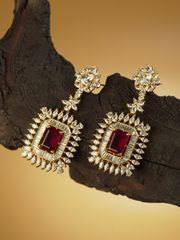 Opulent gold earrings featuring deep red center stones and sparkling diamonds, displayed on a dark wooden surface against a warm golden backdrop.