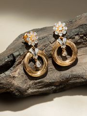 Delicate circular gold earrings featuring floral diamond studs, showcased on a rustic wooden surface in natural light.