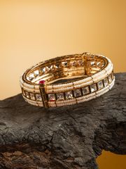 Exquisite gold and pearl bracelet with square-cut stones displayed on a dark wooden surface against a warm golden backdrop