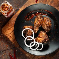 Spicy grilled chicken wings with onion rings on a black plate, garnished with chili flakes