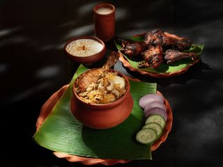 Close-up of a traditional Indian chicken biryani dish on a banana leaf, garnished with onions, cucumbers, and yogurt