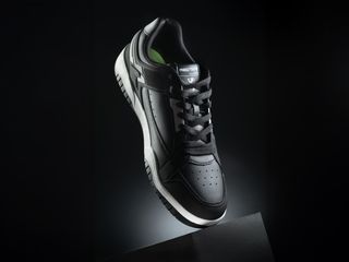 A pair of black sneakers with white soles on a black box against a black background