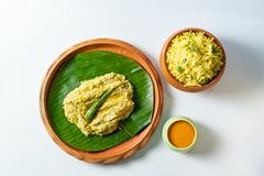 A mustard-marinated fish fillet on a banana leaf in a clay plate, garnished with a green chili, served alongside turmeric rice and a small bowl of sauce.