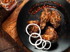 Spicy grilled chicken wings with onion rings on a black plate, garnished with chili flakes