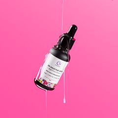 A sleek bottle of face serum with a dropper, displayed on a white pedestal against a vibrant pink background.