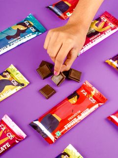 A hand picking up squares of Fancis chocolate from a purple background, surrounded by colorful chocolate bar wrappers.