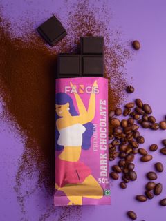 A partially unwrapped Fancis Premium Dark Chocolate bar (50% cocoa) on a purple background, with scattered coffee beans and cocoa powder.