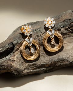 Delicate circular gold earrings featuring floral diamond studs, showcased on a rustic wooden surface in natural light.