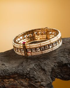 Exquisite gold and pearl bracelet with square-cut stones displayed on a dark wooden surface against a warm golden backdrop