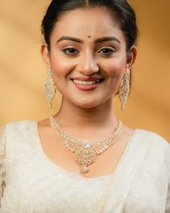 Smiling woman in a white traditional outfit wearing an intricate gold and diamond necklace with matching earrings, set against a warm golden background.