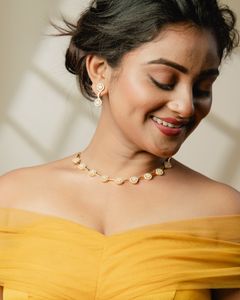 Smiling woman wearing an elegant gold necklace and matching earrings, captured in a warm, softly lit setting.