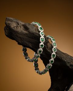 Exquisite diamond and emerald bangles displayed on a rustic wooden branch against a warm golden background.