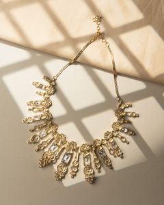 Statement gold necklace adorned with rectangular crystals, showcased in dappled sunlight against a neutral background.