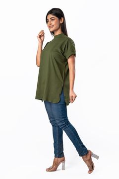 Woman wearing an olive green high‐neck tunic top with rolled sleeves, side slits, and blue skinny jeans, posing in three‐quarter profile.