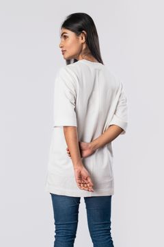 A woman wearing a short-sleeve off-white top from the back, featuring side slits and a comfortable fit, paired with jeans on a neutral background.