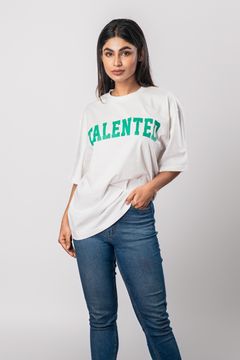 A woman wearing a white T-shirt with green ‘TALENTED’ lettering, paired with jeans, on a neutral background, showcasing a casual style.