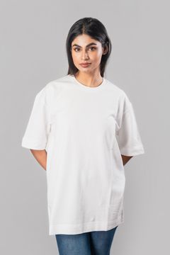 A woman wearing an oversized white short-sleeve T-shirt with a round neckline, paired with jeans on a neutral background, showcasing a casual modern look.