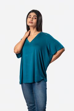 A woman wearing a teal V-neck short-sleeve top with lace shoulder detailing, paired with blue jeans, posing against a white background.