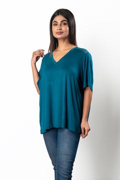 A woman wearing a teal V-neck top with lace shoulder details, paired with jeans on a white background, showcasing a stylish casual look.