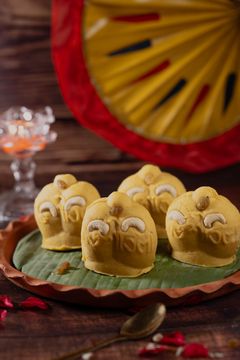 A visually appealing arrangement of yellow sweets on a banana leaf, with a festive background.