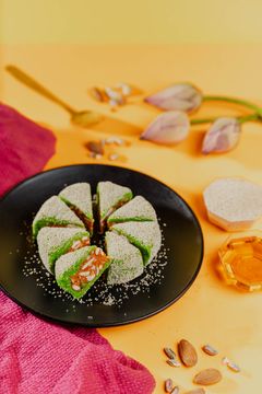 A visually appealing arrangement of green sweets on a black plate, with scattered nuts and a vibrant background.