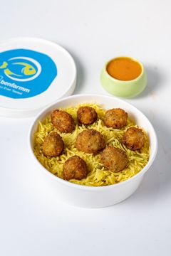 A white container of fish ball biryani topped with golden fried balls, served with a side of tangy sauce.