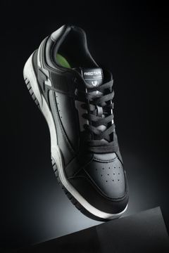 A pair of black sneakers with white soles on a black box against a black background